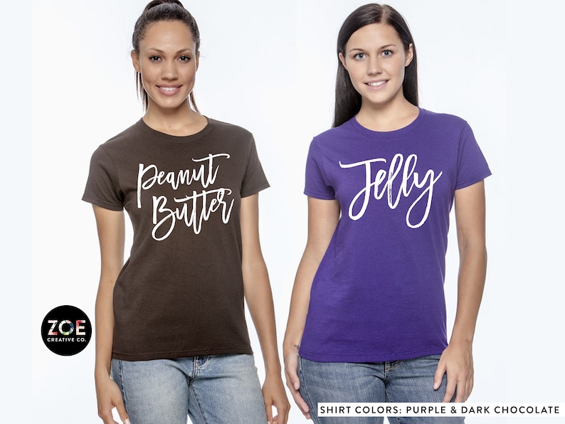 May include: Two women wearing matching t-shirts. One shirt is dark chocolate brown with the text "Peanut Butter" in white. The other shirt is purple with the text "Jelly" in white. The text on the shirts is in a handwritten style font.