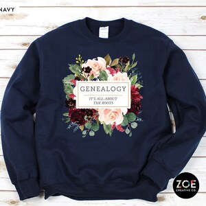 Peut inclure: Sweat-shirt bleu marine avec un motif floral et le texte "Genealogy It's all about the roots".