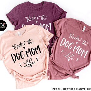 May include: Three t-shirts with the text "Rockin' the Dog Mom Life" in different colors: peach, heather mauve, and heather maroon.