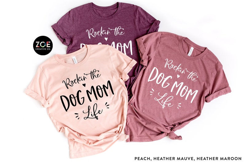 May include: Three t-shirts with the text "Rockin' the Dog Mom Life" in different colors: peach, heather mauve, and heather maroon.