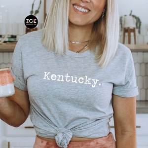 May include: A gray t-shirt with the word "Kentucky." printed in white on the front. The shirt is tied at the waist.