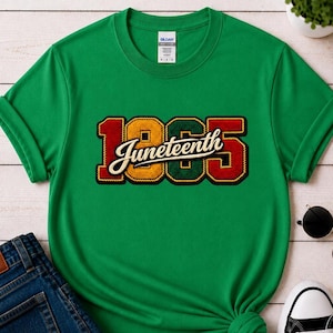 Può includere: Una t-shirt verde brillante a maniche corte con la scritta "Juneteenth" in un carattere corsivo color crema sovrapposta a grandi numeri "1865" in rosso, giallo e verde, con un bordo spesso e scuro simile a una corda.