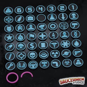 May include: A set of 42 black and blue circular tokens, each with a different icon or number. The tokens include symbols such as a target, a briefcase, a flask, and a gun. Two pink rings are at the bottom. The SaucerMen Studios logo is in the bottom right corner.