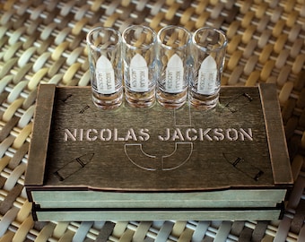 Puede incluir: Una caja de madera con el nombre "Nicolas Jackson" grabado en la parte superior. La caja contiene cuatro vasos de chupito con el mismo nombre impreso en cada uno.