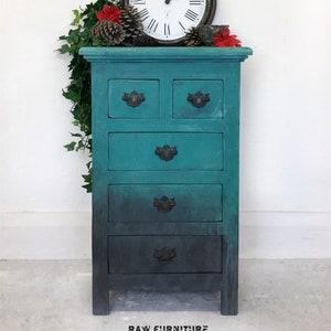 May include: A teal and black chest of drawers with five drawers and antique-style hardware. The chest is decorated with a clock and greenery on top. The text "RAW FURNITURE" is printed on the bottom of the image.