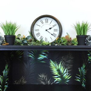May include: Black shelf unit with a tropical leaf pattern wallpaper lining the shelves. The shelf is decorated with potted plants, a clock, and other decorative items.