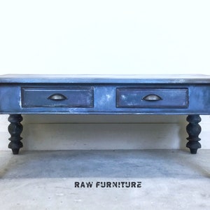 May include: A blue coffee table with two drawers and turned legs. The table has a distressed finish and black metal drawer pulls. The table is labelled "RAW FURNITURE".