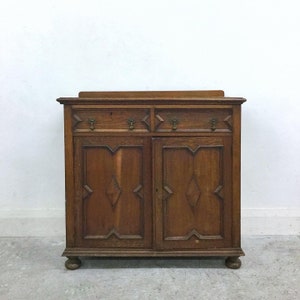 Op de afbeelding: Een vintage houten kast met twee lades en twee deuren. De kast heeft een donkerbruine afwerking en heeft diamantvormige carving op de deuren.