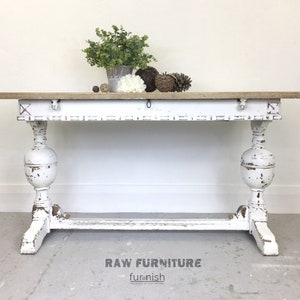 May include: White distressed wood console table with a distressed wood top and turned legs. The table is decorated with a small potted plant and decorative items. RAW FURNITURE furnish.