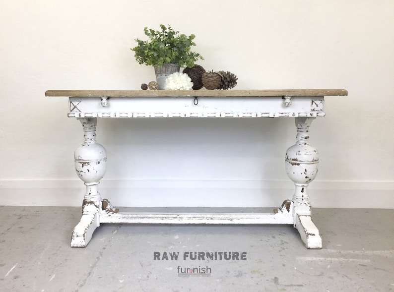 Op de afbeelding: Witte, verweerde houten consoletafel met een verweerd houten blad en gedraaide poten. De tafel is versierd met een kleine plant in een pot en decoratieve items. RAW FURNITURE furnish.