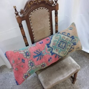 May include: A wooden chair with a carved back and a patterned pillow. The pillow is a long, rectangular shape and has a red, blue, and green design.