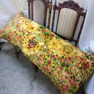 May include: A long, yellow floral patterned pillow with red, green, and gold accents. The pillow is resting on a wooden bench with a carved back.