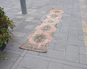 May include: A long, pink and cream colored rug with a floral pattern. The rug is lying on a gray concrete surface.