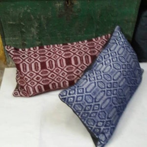 Op de afbeelding: Twee decoratieve kussens met geometrische patronen. Het ene kussen is rood en wit, het andere is blauw en wit.