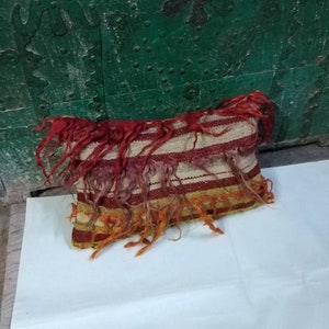 May include: A rectangular pillow with a striped pattern in red, white, and yellow. The pillow has a fringe border and is made of a woven fabric.