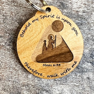 May include: Wooden keychain with a religious theme. The round keychain features a laser-cut design of two figures and a sun, with the text "Behold my Spirit is upon you. Therefore, walk with me. Moses 6:34."