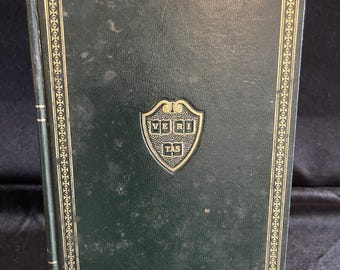 May include: A dark green book with gold trim and a gold emblem. The book has a leather-like texture and a decorative border. The emblem features the text "VERI TAS".