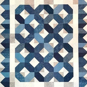 May include: A handmade quilt featuring a geometric pattern in various shades of blue and white. The design includes interlocking shapes and a border with a sawtooth edge. The quilt is likely made of cotton fabric.