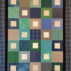 May include: A quilt with a black border and a patchwork design. The quilt is made up of squares of different colors and patterns, including green, blue, brown, and white. The squares are arranged in a grid pattern.
