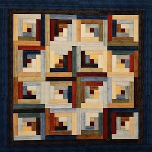 May include: A handcrafted quilt with a log cabin design. The quilt features a repeating pattern of squares in various colors, including shades of blue, brown, beige, and red. The quilt is framed by a dark blue border.