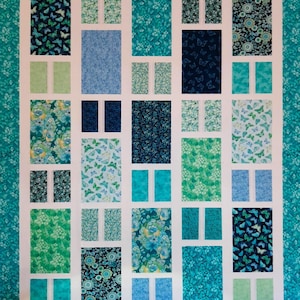 May include: A patchwork quilt with a geometric design. The quilt features rectangular blocks in shades of blue, teal, and green, with various floral and butterfly patterns. The blocks are separated by white borders, and the edges are bordered with a teal floral pattern.