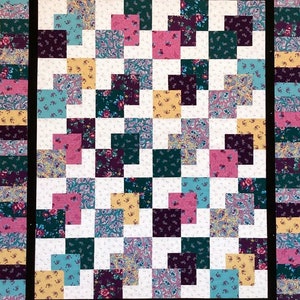 May include: A quilt with a patchwork design featuring a variety of floral and paisley patterns in shades of pink, teal, yellow, and purple. The quilt is framed with a black border and a multi-colored border.