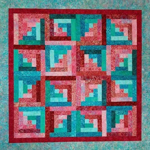 May include: A quilt with a log cabin pattern in shades of pink, red, and teal. The quilt is made up of squares with a border of red and teal.