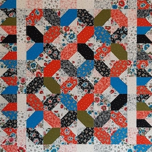 May include: A colorful quilt with a repeating pattern of angled blocks in red, black, blue, and olive green. The blocks are set against a white background with floral and patterned fabric accents. The quilt has a decorative border.