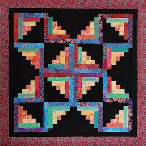 Peut inclure: Un bloc de courtepointe coloré avec un motif de cabane en rondins dans des tons de rouge, orange, jaune, vert, bleu et violet. Le bloc est placé sur un fond noir.