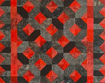 May include: A handmade quilt with a geometric pattern in shades of red, black, and grey. The quilt features diamond and square shapes, with a red border and a repeating triangle pattern along the edges. The fabric has a textured appearance.