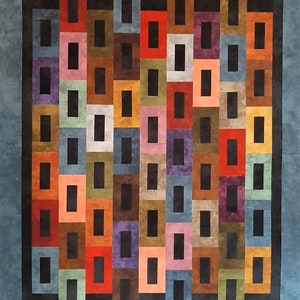 May include: A colorful quilt with a geometric pattern of squares and rectangles. The quilt is made up of various shades of red, orange, yellow, green, blue, purple, and brown. The squares and rectangles are arranged in a repeating pattern, creating a visually appealing design.