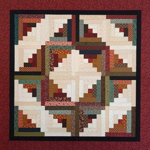 May include: A quilt with a log cabin pattern in shades of brown, red, green, and cream. The quilt is framed with a black border and a red border.