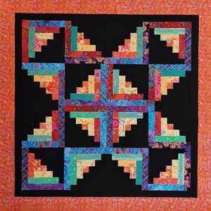 May include: A colorful quilt block with a log cabin pattern in shades of red, orange, yellow, green, blue, and purple. The block is set against a black background.