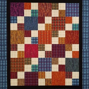 May include: A quilt with a patchwork design featuring squares of various colors and patterns, including red, blue, brown, and white. The quilt is framed with a black border and a blue border.