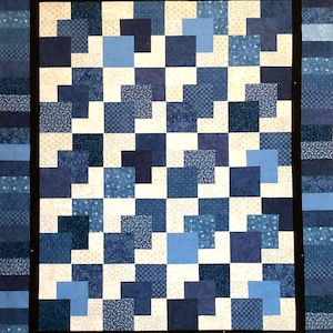 May include: A handmade quilt featuring a patchwork design in shades of blue and white. The quilt has a black border and a repeating pattern of squares and rectangles. The fabrics have various patterns, including floral and geometric designs.