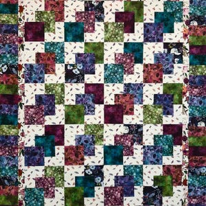 Może przedstawiać: Kołdra w patchworkowym wzorze z kwadratami w różnych wzorach kwiatowych w odcieniach fioletu, zieleni, błękitu i czerwieni. Kwadraty są ułożone w przesunięty wzór na białym tle z kwiatową ramką.