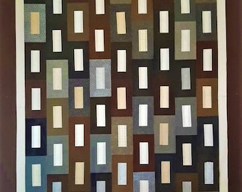 May include: A quilt featuring a geometric design of squares and rectangles in shades of brown, beige, and blue. The quilt is constructed from various fabrics, each with a distinct texture and pattern.