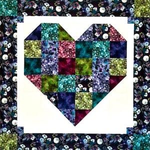 May include: A quilted heart design with a patchwork center in shades of teal, purple, green, and burgundy. The heart is framed by a white border and surrounded by a floral patterned fabric in dark blue and white.