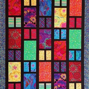 Op de afbeelding: Een kleurrijk quilt met een patchwork-ontwerp met verschillende bloemenpatronen en geometrische vormen. De quilt is gemaakt van vierkanten en rechthoeken, met een zwarte rand rond de randen.