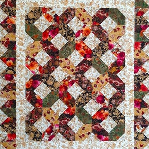 May include: A handmade quilt with a repeating pattern of interlocking shapes in shades of red, green, brown, and gold. The quilt features floral and paisley prints, with a white floral border and a sawtooth edge.