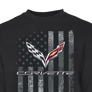 May include: Black sweatshirt featuring a distressed American flag design with the Corvette logo. The flag has gray and white stripes with a field of stars. The Corvette logo is in silver, red, and black.