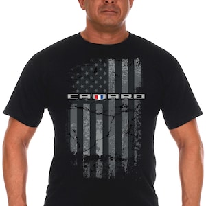 May include: A black t-shirt with a distressed American flag design and the word "CAMARO" printed on it. The flag is in shades of gray and black with a red, white, and blue Camaro logo.