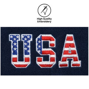 May include: Embroidered "USA" text in red, white, and blue, with the stars and stripes design. The letters are stitched onto a navy blue fabric. The image also includes a circular logo with the text "High Quality Embroidery".