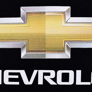 Pode incluir: Um logotipo Chevrolet prateado e dourado com a palavra "CHEVROLET" em letras brancas abaixo.