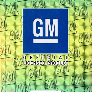 Pode incluir: Uma etiqueta de pendurar azul com um logotipo "GM" branco e o texto "PRODUTO OFICIAL LICENCIADO". O fundo &eacute; um padr&atilde;o hologr&aacute;fico verde e azul com o logotipo "GM" repetido.