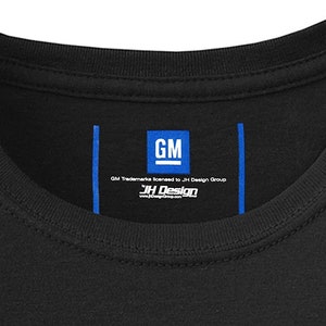 Pode incluir: Uma camiseta preta com uma etiqueta azul que diz "GM Trademarks licensed to JH Design Group" e "JH Design" com um endere&ccedil;o de site.