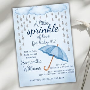 May include: Baby shower invitation with a light blue background, featuring the text "A little sprinkle of love for baby #2." The design includes a blue umbrella, clouds, and raindrop accents. Details include the date, time, and location.