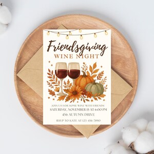 Puede incluir: Una tarjeta de invitaci&oacute;n para una Friendsgiving Wine Night, con copas de vino, calabazas y hojas de oto&ntilde;o. La tarjeta est&aacute; sobre un plato de madera con un sobre. El texto dice "Friendsgiving Wine Night" y los detalles del evento.