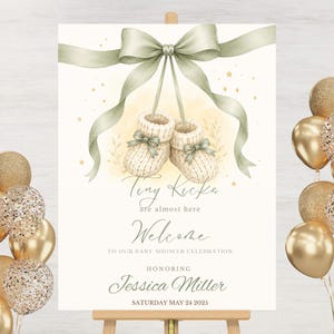 May include: A rectangular baby shower welcome sign featuring a watercolor illustration of two cream-colored knit baby booties tied with a sage green ribbon. The text reads: Tiny Kicks are almost here, Welcome TO OUR BABY SHOWER CELEBRATION HONORING Jessica Miller SATURDAY MAY 24 2025.
