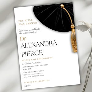 May include: A white graduation invitation card featuring a black velvet tam with a gold tassel at the top right. The text reads: THE TITLE WAS EARNED, Join us as we celebrate the achievement of Dr. ALEXANDRA PIERCE, DOCTOR OF PHILOSOPHY in Clinical Psychology, SATURDAY, JUNE 14, 2025, 4:00 PM, THE HERITAGE ROOM, 123 CELEBRATION LANE, ATLANTA, GEORGIA 30309, DINNER & CELEBRATION to follow.